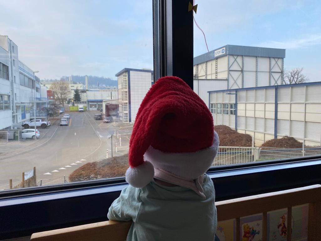 Kind schaut mit Weihnachtsmütze aus dem Fenster in der Kinderkrippe Stärnschnuppe
