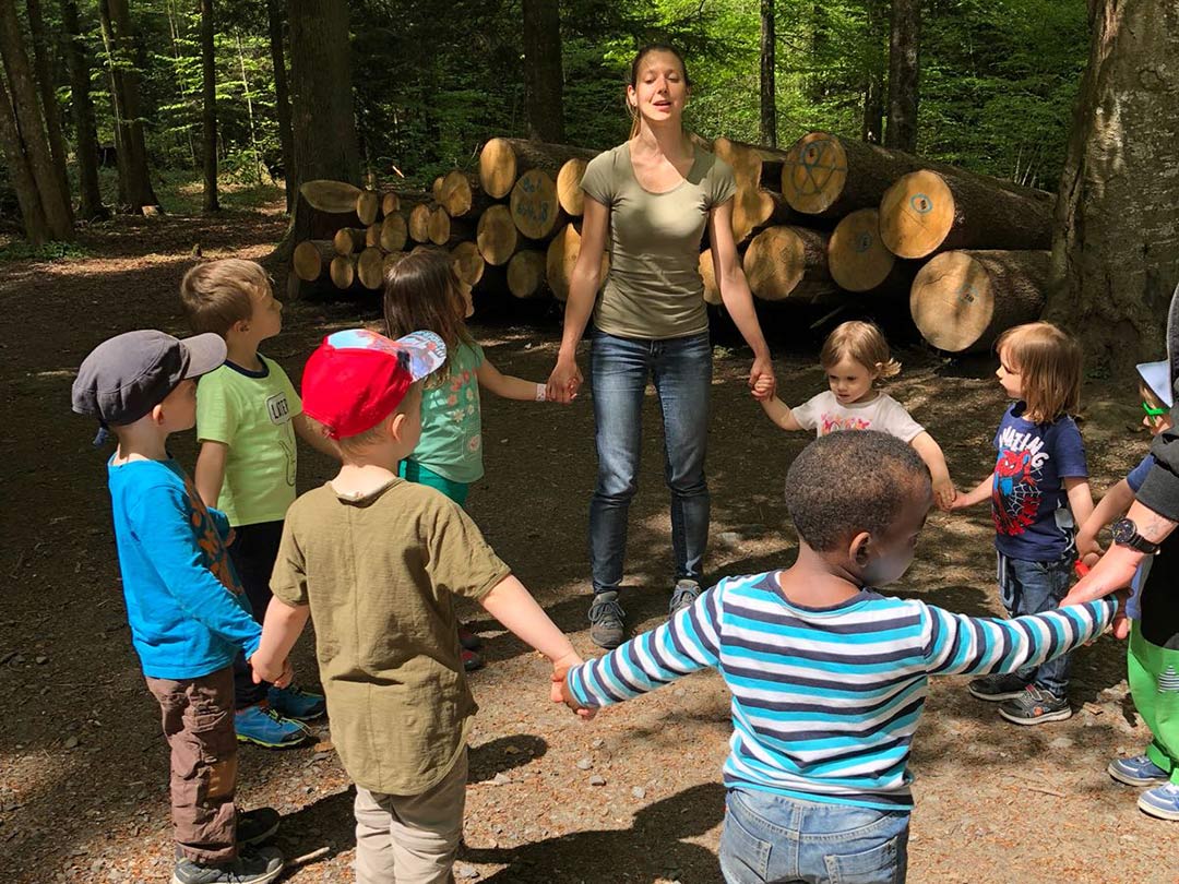 Kinder und Betreuerin singen im Kreis im Wald in der Waldgruppe der Kinderkrippe Stärnschnuppe